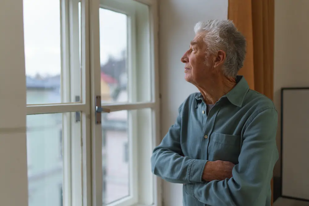 Senior man looking out the window, with lack of purpose.